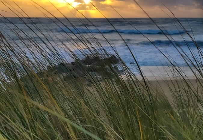 the sun is setting over the ocean and the beach