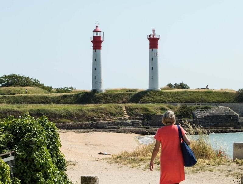 a woman in a red dress is walking towards two lighthouses